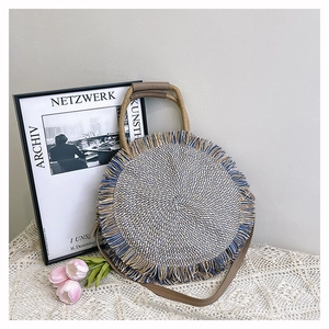 Detailed close-up of a handwoven round straw bag with blue fringe and leather strap
