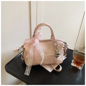 Close-up of pink Boston bag with embossed logo, lace ribbon, and heart pendant detail