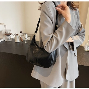 Detail of a black hobo bag with gold buckle on a brown leather shoulder strap