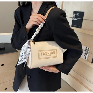 Detail of cream shoulder bag featuring an elegant silk scarf braided strap and embossed logo