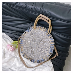 Detail shot of a round woven straw bag featuring blue fringe trim and leather handles