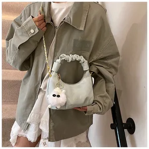 Detail of light blue pleated croissant bag with gold chain strap and white plush charm