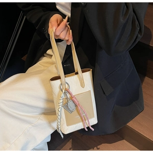 Detail of cream tote bag with khaki pocket, metal tennis charm and braided rope accent