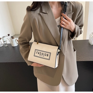 Modern beige crossbody bag with black leather trim and artistic lettering in a cafe setting