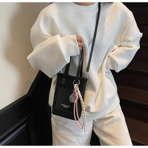 Detail of black leather crossbody bag with woven knot charm and metal grid pendant