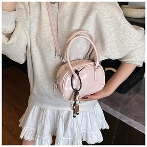 Pale pink glossy bowling bag with cute doll charm shown as a crossbody on model