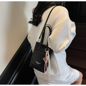 Detail view of black bucket bag with contrast knot charm and fashion logo print