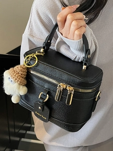 Minimalist black box handbag in lychee leather with gold zippers and a knit hat charm