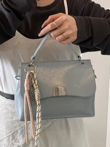 Light blue-grey soft leather tote bag with flap closure and colorful woven pendant