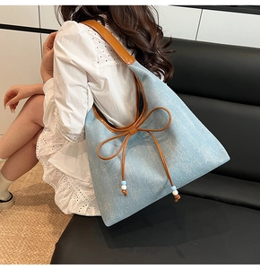 Modella che indossa una borsa tote in denim celeste con spalline in pelle marrone e ciondolo