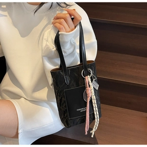 Detail view of black pleated bucket bag with decorative woven pendant and front pocket