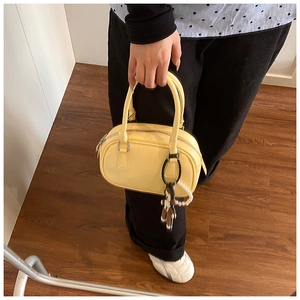 Detail of pale yellow glossy bowling bag featuring pearl chain and cartoon charm accessory