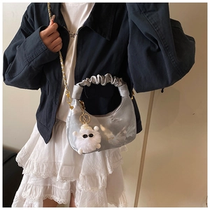 Detail of silver crescent bag featuring pleated handle, gold chain and plush charm