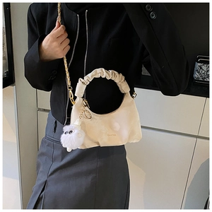Detailed shot of cream pleated dumpling bag with gold chain and plush charm