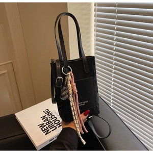 Detail of black textured leather mini tote with metal racket charm and woven knot