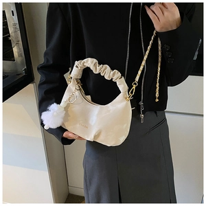 Detail view of off-white pleated hobo bag featuring golden chain strap and plush pom-pom charm