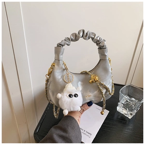 Detail of silver pleated handbag featuring golden leather chain and plush monster charm