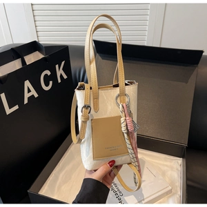 Detail of a minimalist cream crossbody bag with a brown contrast pocket and a knotted charm