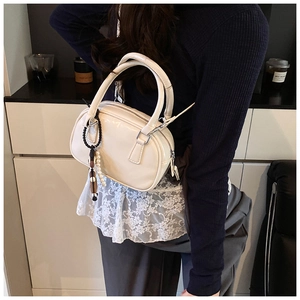 Detail view of white patent leather bowling bag with pearl charm and silver zipper closure