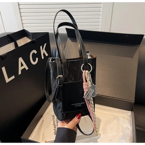 Detail of a black mini tote bag in crinkled leather with fashion tags and handle charms