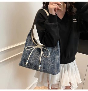 Dettaglio della borsa hobo in denim blu con fiocco in pelle bianca e perline decorative