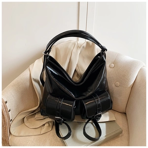Close-up of black glossy tote bag with dual front flap pockets on a beige leather chair