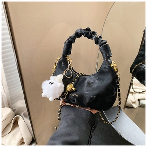 Detail of black crescent handbag with gold chain, pleated handle and plush lamb charm