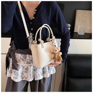 Detail van een crème bucket bag met geknoopte handgreep en teddybeer hanger