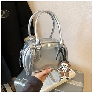 Detail of silver metallic handbag with round handles and brown cartoon charm accessory