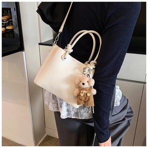 Elegante beige bucket bag met teddybeer-bedeltje, getoond in een moderne lifestyle-omgeving