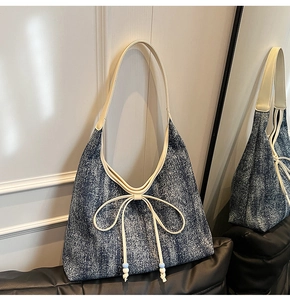 Dettaglio della borsa hobo in denim blu con tracolla in pelle bianca e fiocco elegante