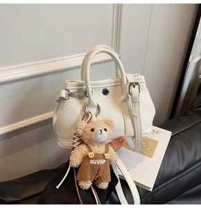 Detalle del bolso de cuero blanco con patrón de lichi y un colgante de oso de peluche