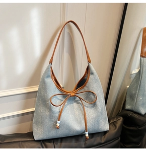 Dettaglio della borsa tote in denim azzurro con fiocco in pelle marrone e ciondolo