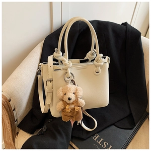 Detail van gebroken witte leren emmertas met zilveren ringen en een teddybeer hanger
