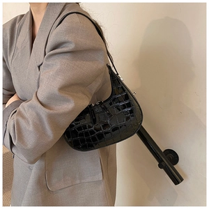 Close-up of black crocodile pattern patent leather shoulder bag on a model wearing a grey suit