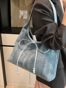 Borsa a spalla in denim blu con fiocco e perline indossata da una modella donna