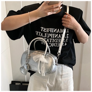 Détail d'un sac à main argenté avec nœud en dentelle et breloque en forme de cœur