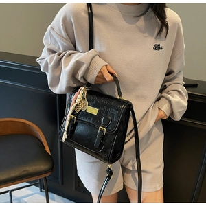 Gros plan d'un sac à main noir gaufré avec foulard en soie et plaque métallique