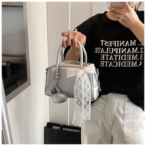 Sac oreiller argenté métallisé avec nœud en dentelle blanche et pendentif cœur tenu à la main