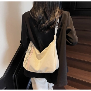 Detail of soft cream hobo tote bag featuring a decorative pink rope knot and tassel