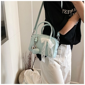 Détail du sac Boston bleu clair avec nœud en dentelle et breloque cœur sur la bandoulière