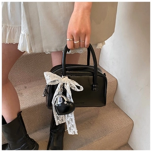 Détail du sac polochon vernis noir avec breloque en dentelle et poignées à boules
