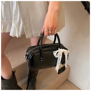 Détail du sac bowling noir brillant avec un pendentif nœud en dentelle blanche