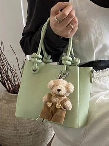 Minimalistische lichtgroene emmertas van leer met knoopgreep en een teddybeer hanger