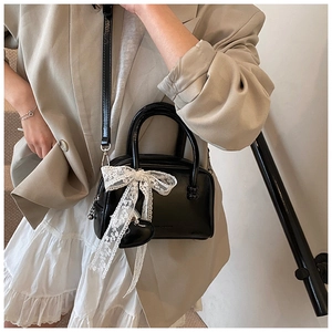Détail du sac en cuir noir brillant avec un nœud en dentelle et pendentif en cœur