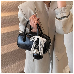 Détail du mini sac bowling en cuir verni noir avec nœud en dentelle blanche et cœur argenté