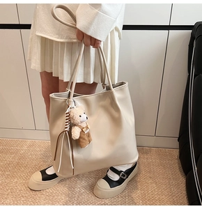 Detail of beige faux leather tote bag with a cute bear charm in a modern interior setting