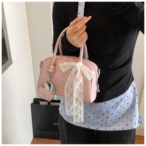 Vue détaillée du sac à main rose en cuir avec nœud en dentelle blanche et pendentif coeur argent