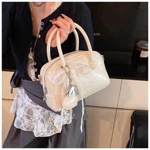 Détail du sac polochon crème brillant avec nœud en dentelle et pendentif cœur argenté