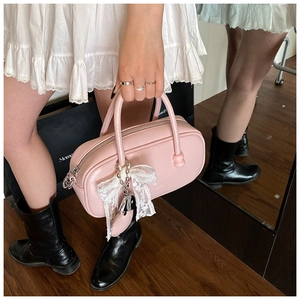 Détail du sac bowling en cuir rose clair avec nœud en dentelle blanche et pendentif cœur